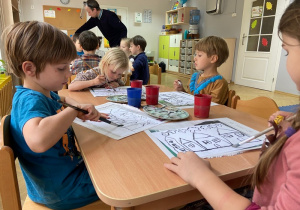 Dzieci siedzą przy stoliku i malują farbami na zajęciach plastycznych